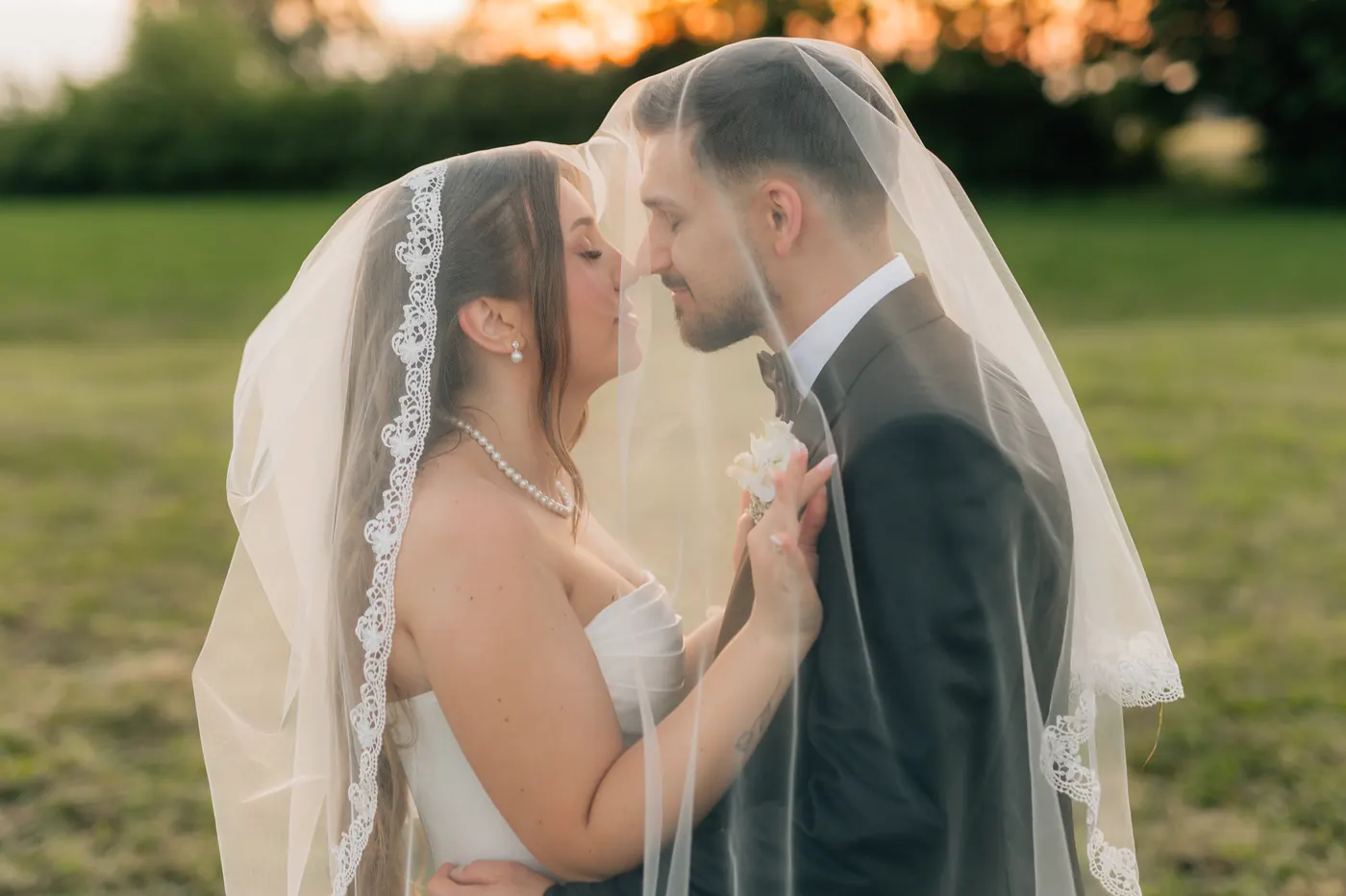 Para młoda pod jednym welonem, za nimi zachodzące słońce